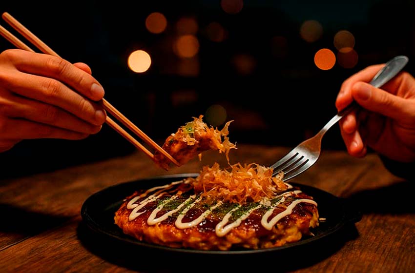 Persona comiendo okonomiyaki japonés en un restaurante nocturno